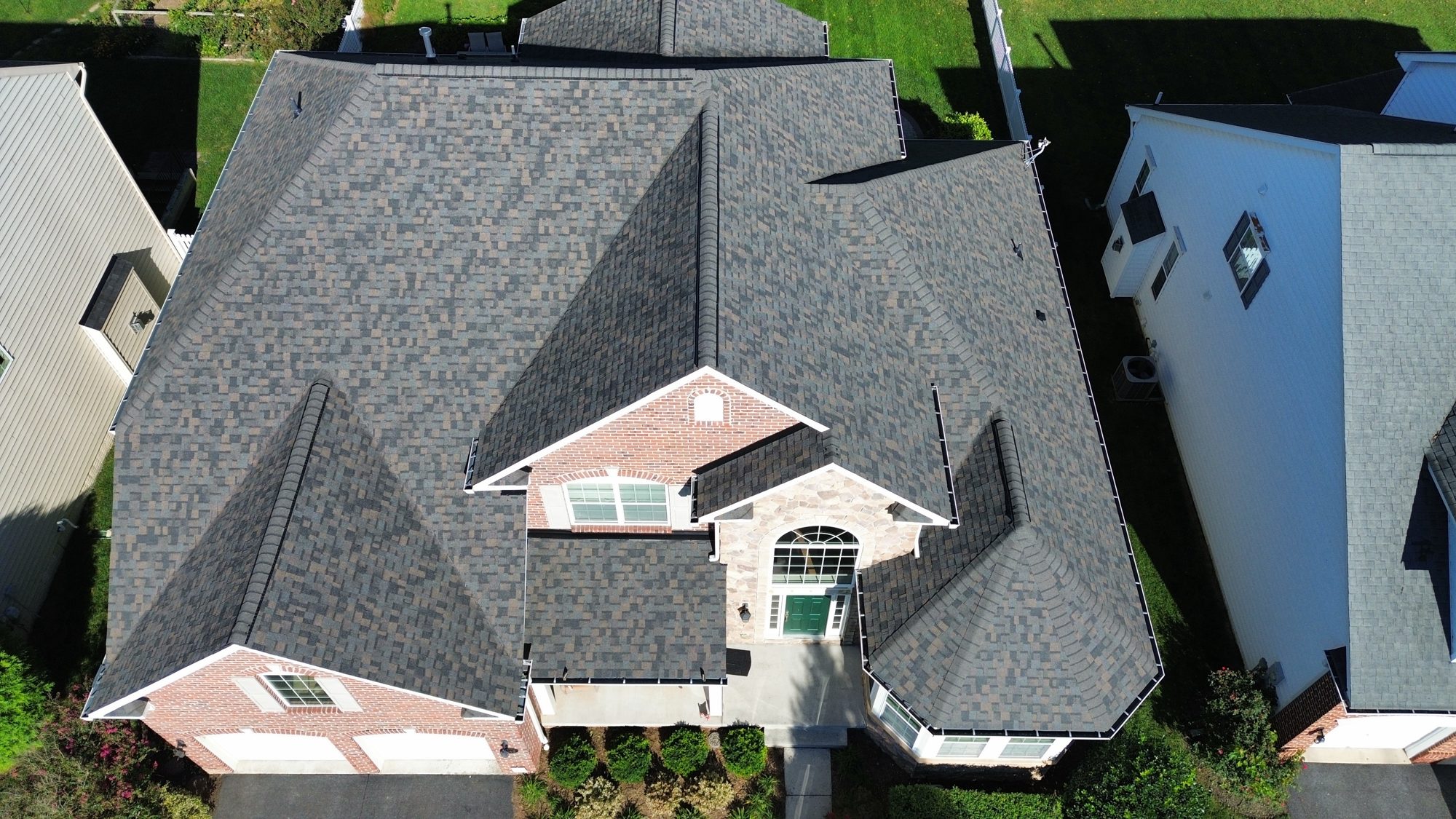 Aerial view of a completed Kelly Home Improvements roof replacement on a brick and stone home